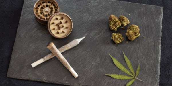 Marijuana joints, dried cannabis buds, and a marijuana leaf on a flat surface